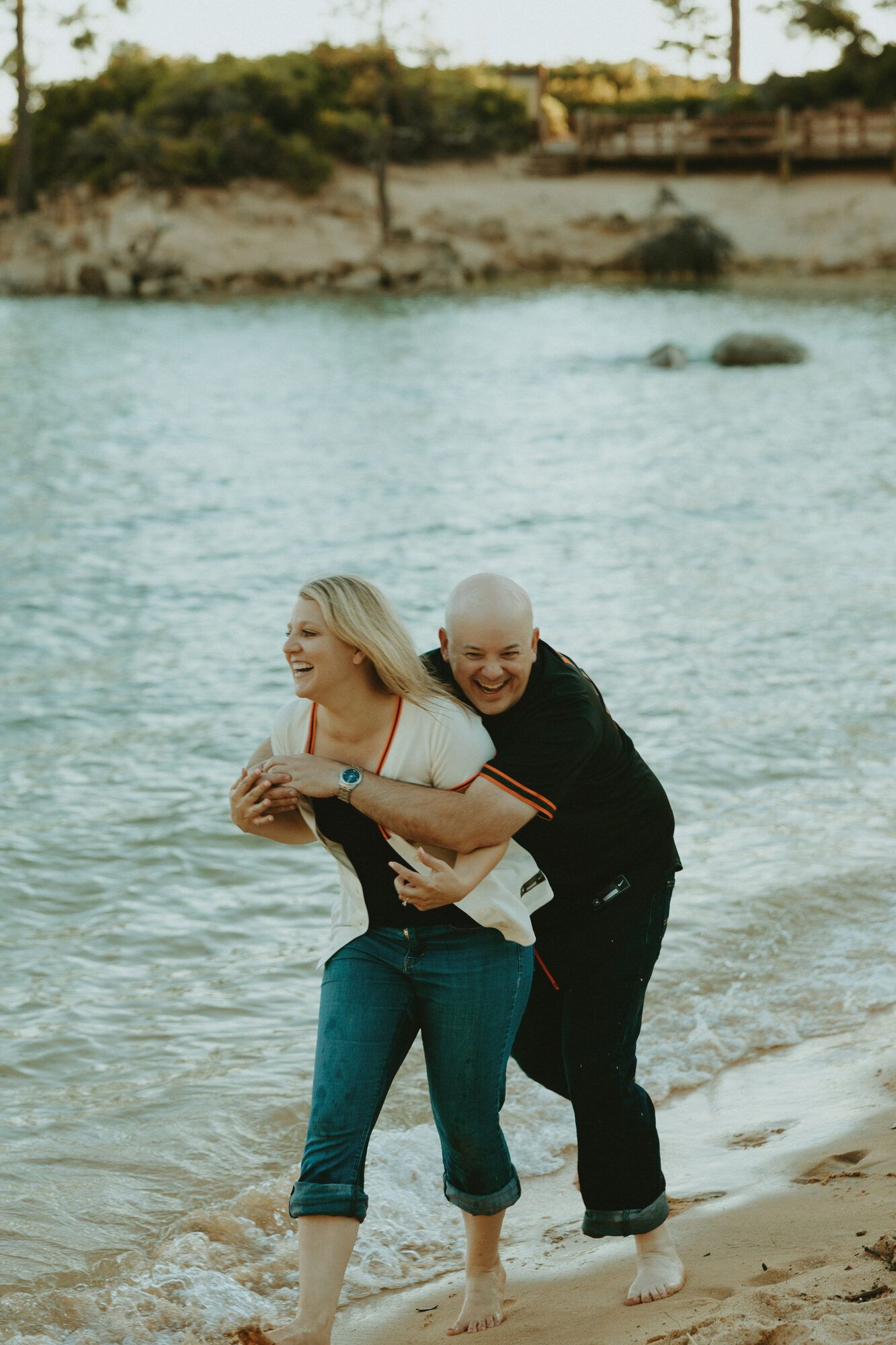 A hug from behind, both laughing by the water